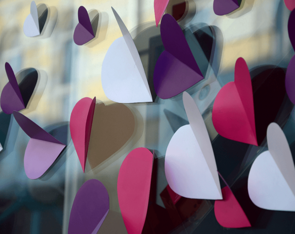 Several purple, red, and white cut paper hearts on a window.